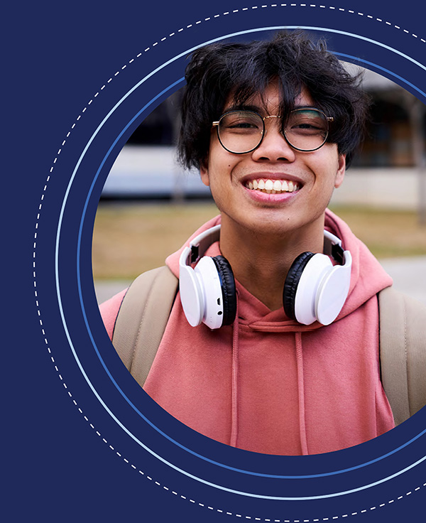 A smiling young person with a pink hoodie, glasses and white headphones around their neck