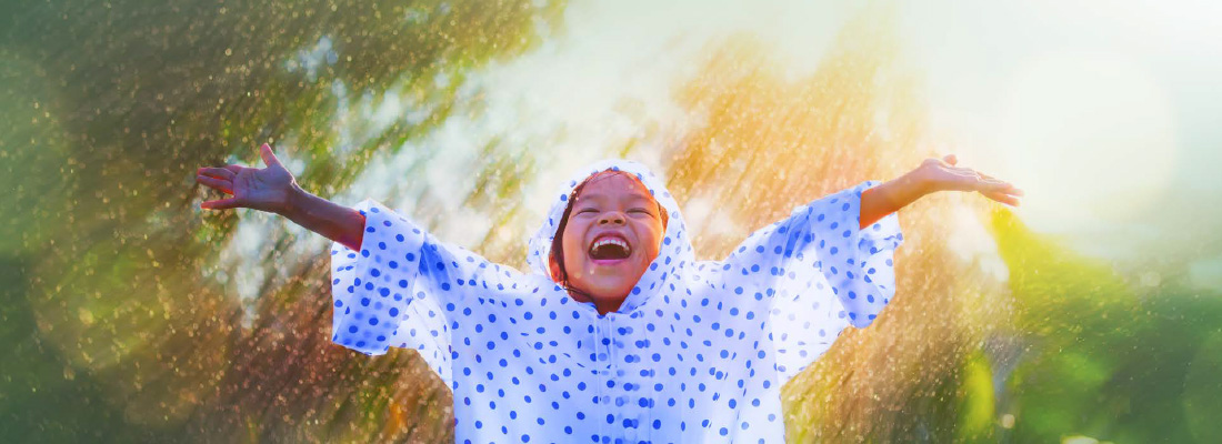 • Smiling child in a raincoat standing with arms outstretched in the sun and rain