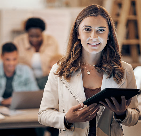 A student stands holding a tablet while her group works in the background