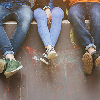 The legs of three young people sitting on a skatepark ledge