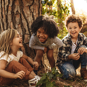 Three laughing children sitting by a tree