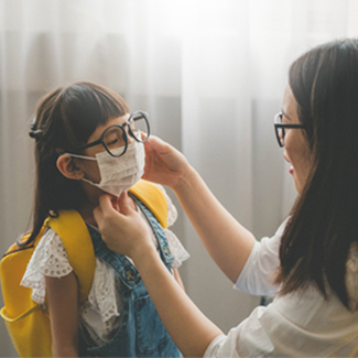 A mother helps her daughter put on a protective face mask