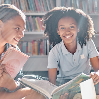 Deux jeunes sont assis dans une bibliothèque tenant des livres et souriant