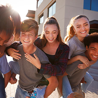 Six youth piggybacking in front of university buildings