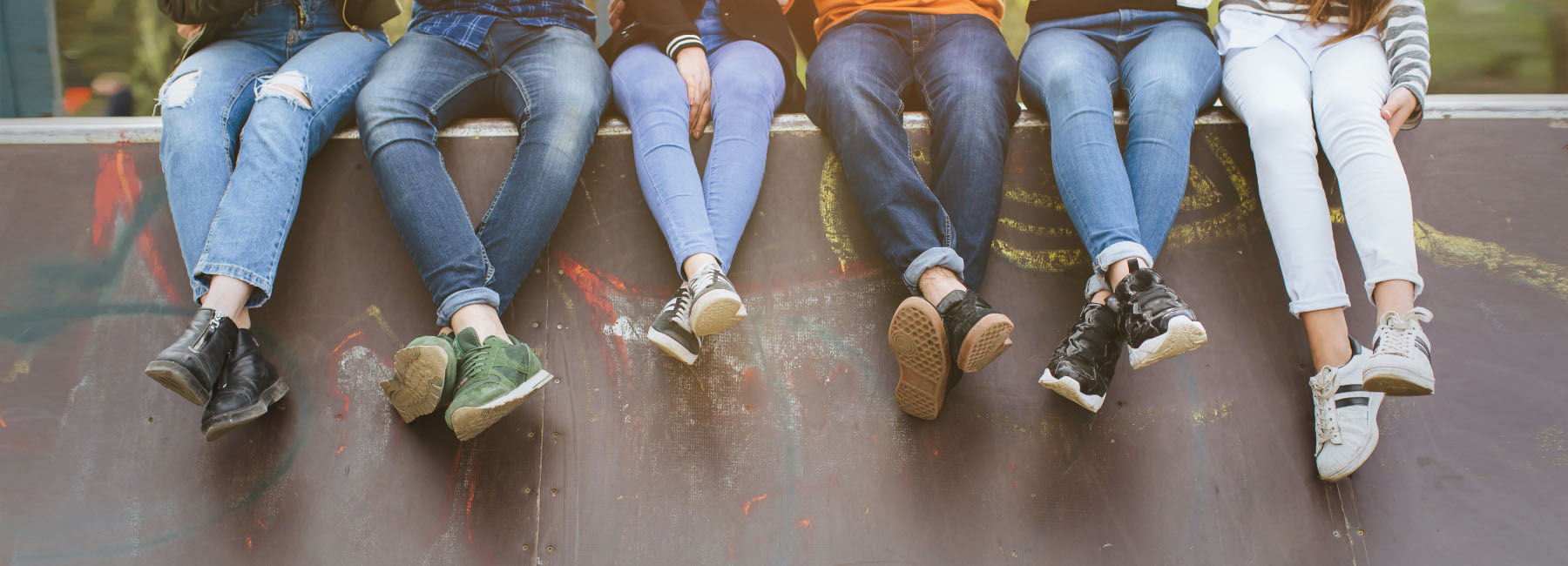 The legs of five young people sitting on a skatepark ledge