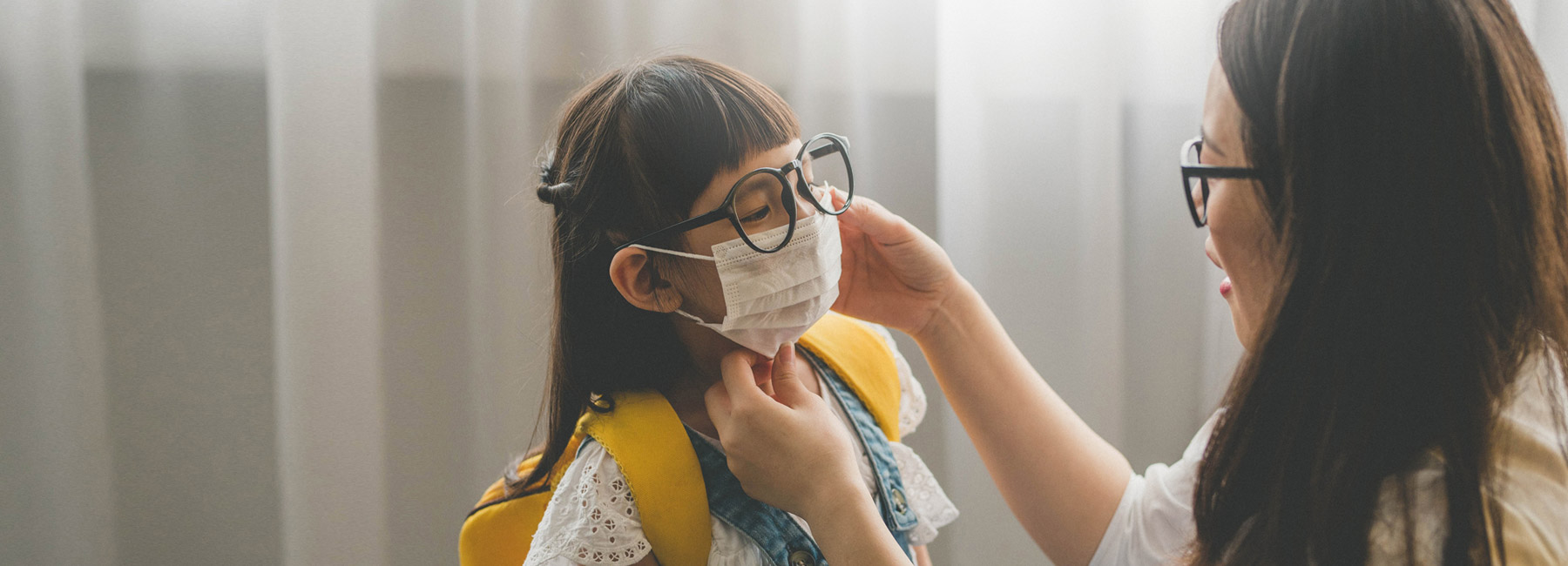 A mother helps her daughter put on a protective face mask