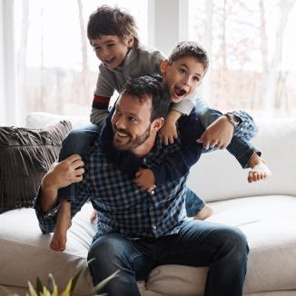 Un homme souriant est assis sur un canapé avec deux jeunes garçons joyeux sur son dos.