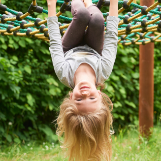 Un jeune enfant est suspendu par les genoux à une structure d'escalade en plein air